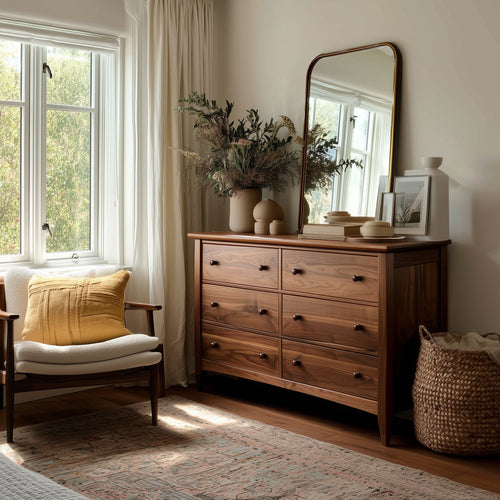 Wooden dresser with mirror in a room with a window, chair, and decorative items.