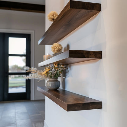 A series of walnut floating shelves mounted on a wall, holding decorative items like a small potted plant and a framed picture.